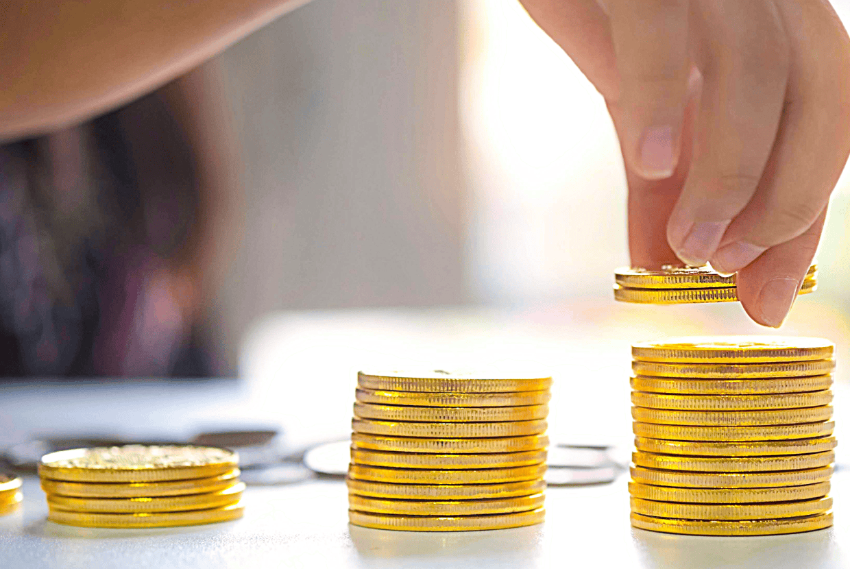 Hand placing coins onto a stack of gold coins, showing increasing piles that represent saving money, growth and financial progress.
