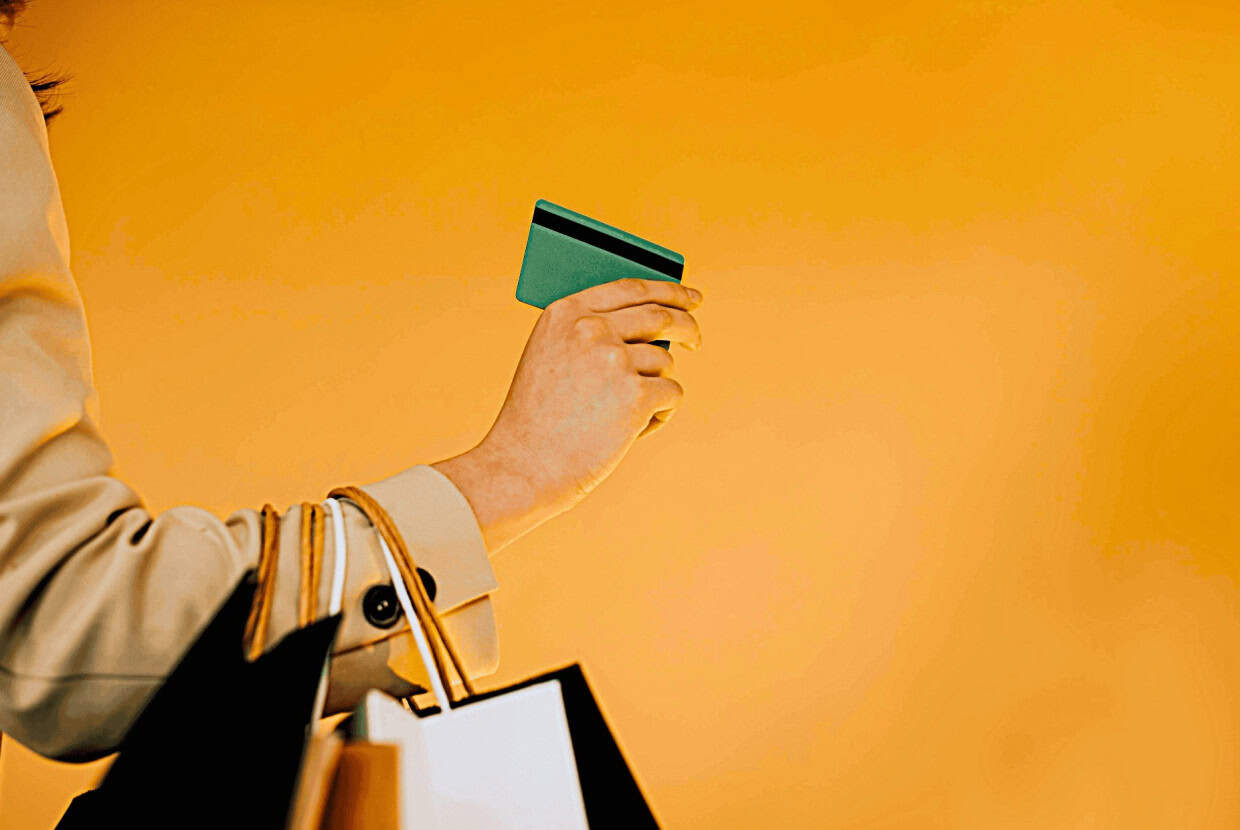 Person holding a credit card while carrying shopping bags against a bright background.