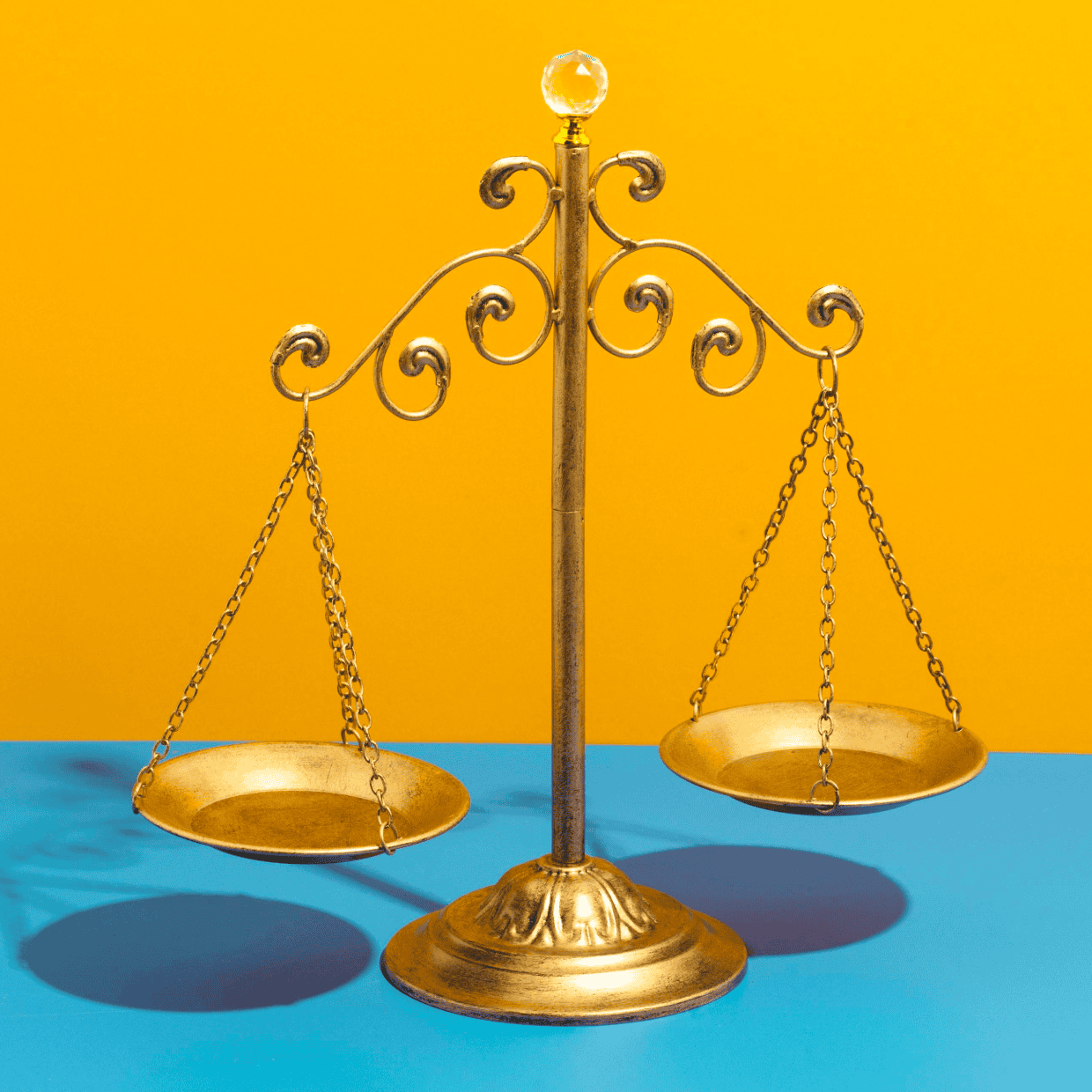 Decorative golden balance scales standing on a blue surface against a bright yellow background.