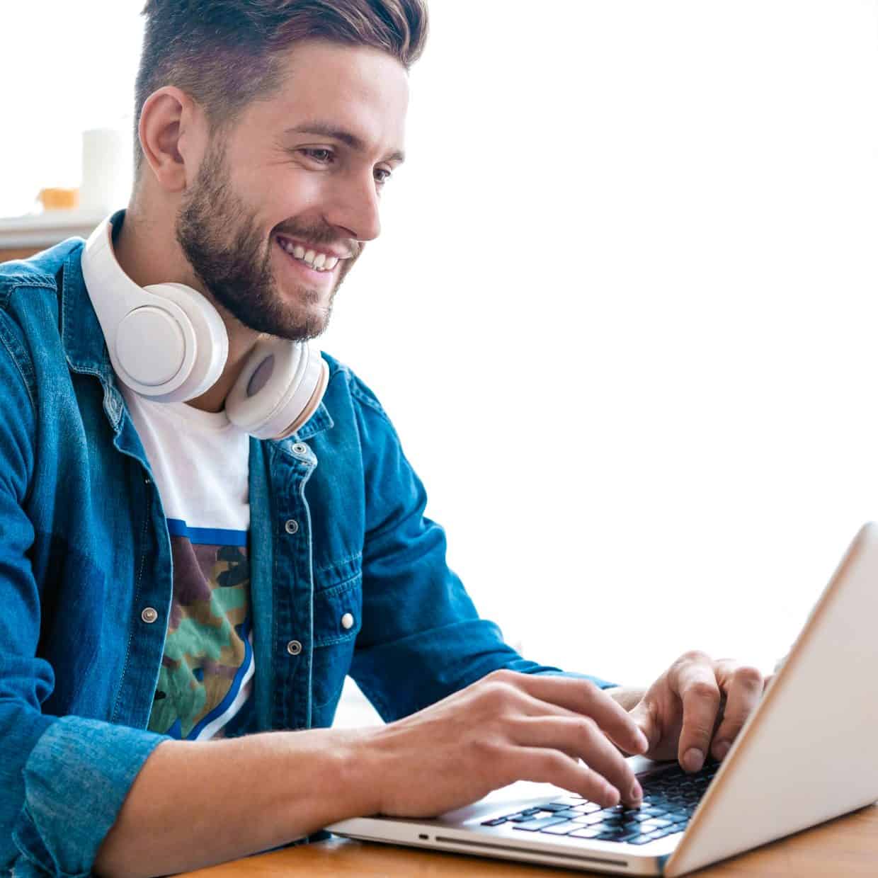Man smiling while working on a laptop, with headphones resting around his neck.