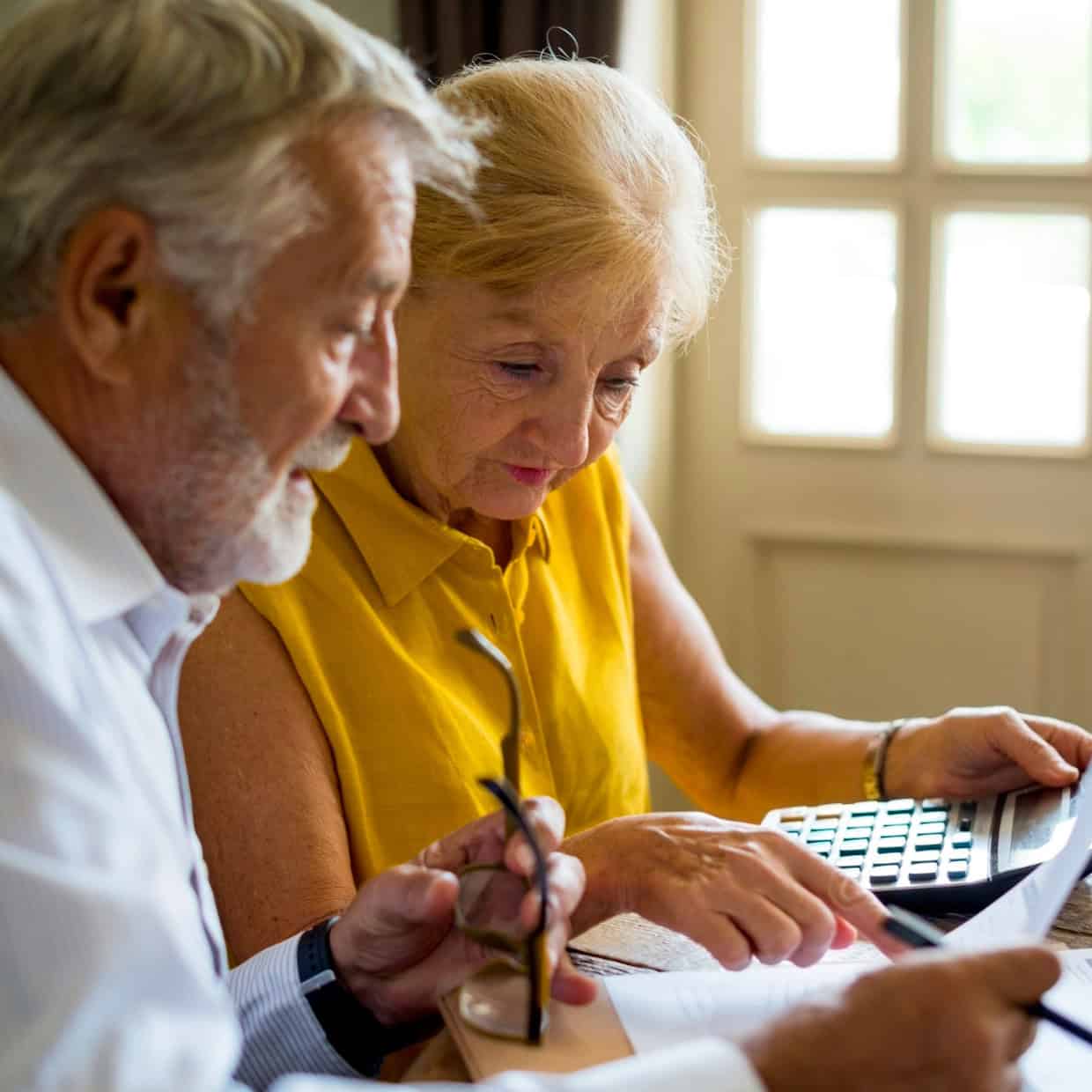 Couple sitting at a table reviewing financial documents together, with a calculator and papers spread out in front of them.