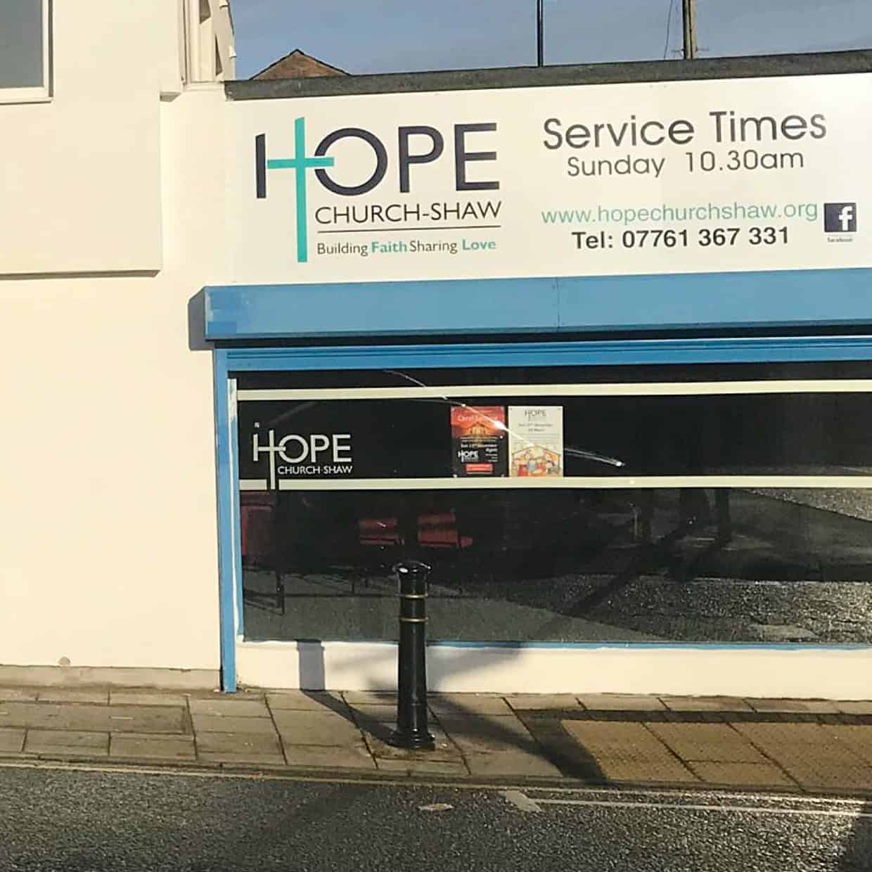 Exterior of Hope Church Shaw building with signage displaying service time of Sunday 10:30am, website address, and contact number above a blue-framed window.