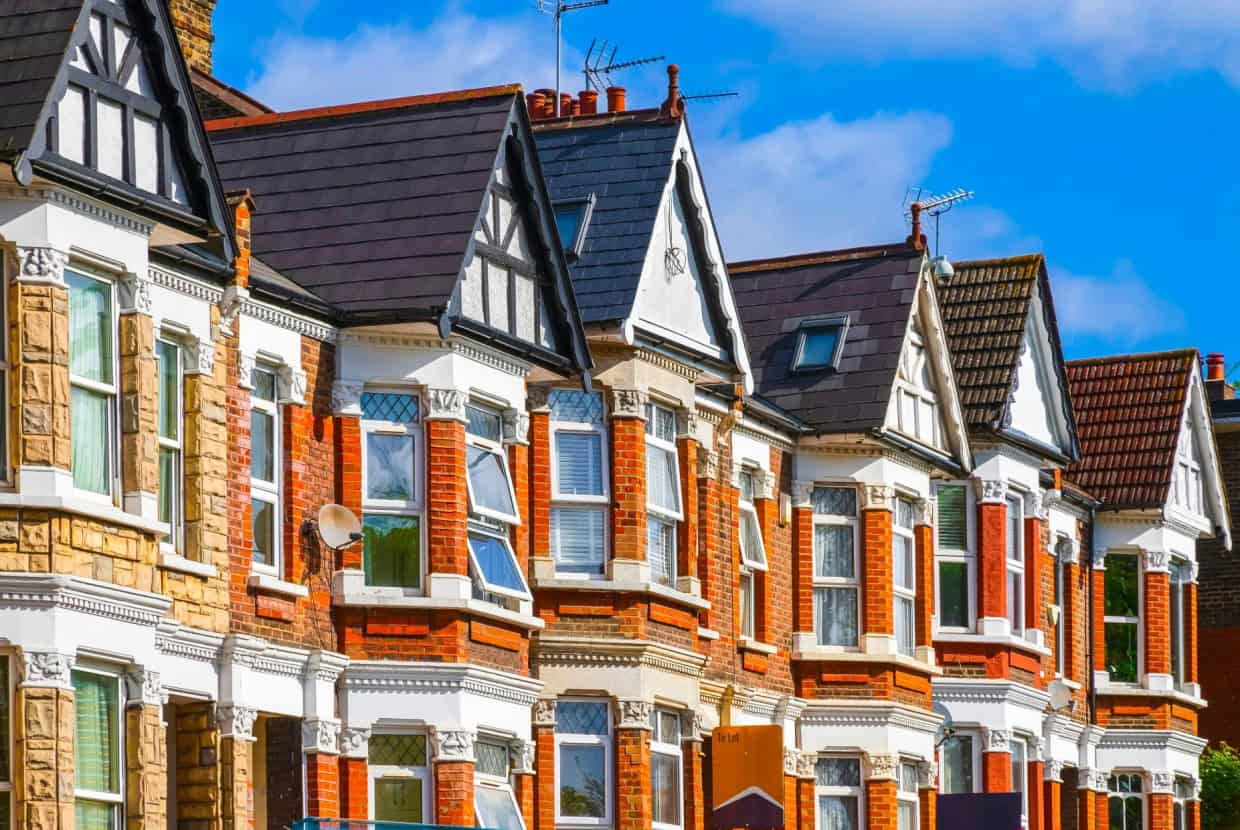 Row of Victorian terraced houses in the UK with red brick façades, bay windows, pitched slate roofs and decorative gables under a blue sky.