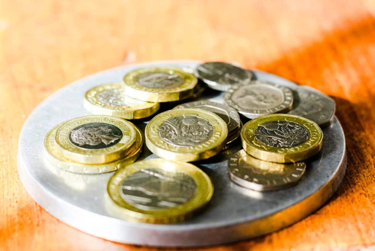 Close-up of British pound coins and small change stacked on a round metal tray on a wooden surface.