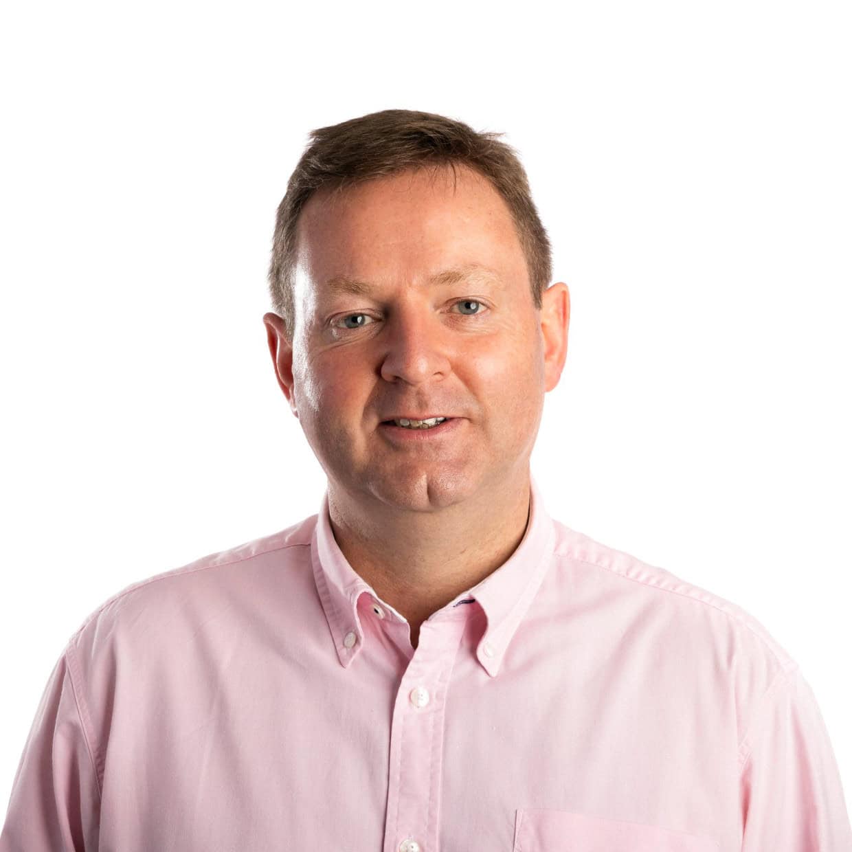 Man wearing a light pink button-up shirt smiling against a plain white background.