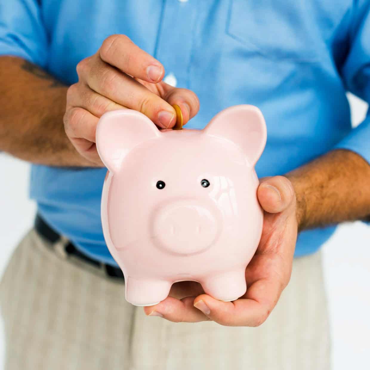 Man wearing a blue shirt placing a coin into a pink piggy bank, symbolising saving money.