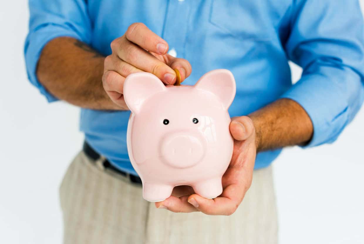 Man wearing a blue shirt placing a coin into a pink piggy bank, symbolising saving money.